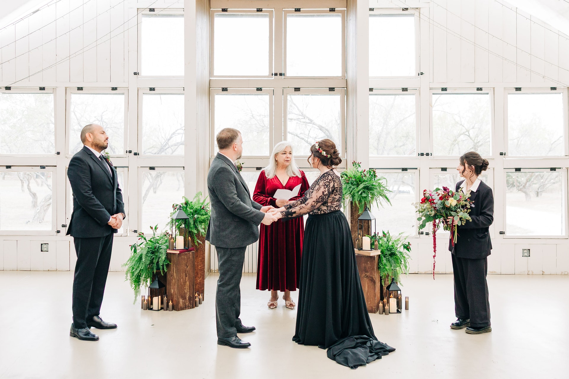 Billy & Jenn standing at the ceremony, with Jenn's daugher on her side and Billy's best man on his. They look towards the officiant with a backdrop of the large square windows of Camino Real