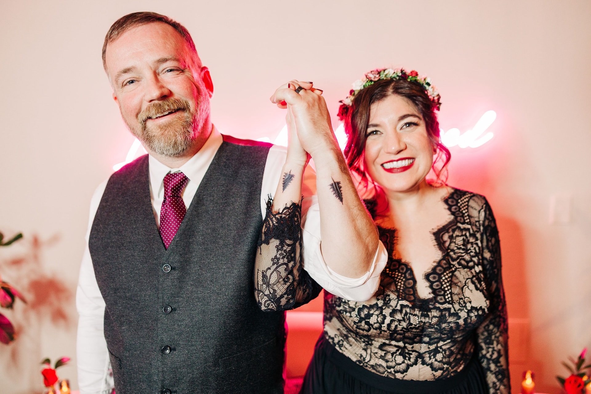 Billy & Jenn showing off their new matching tattoos of the silouette of a tall tree, done on their wrists. Both are smiling and looking at the camera while holding hands with the tattoos on their wrists.