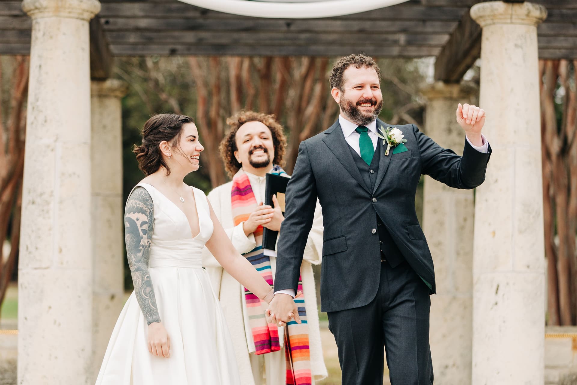 A couple smiling towards the crowd after their ceremony concluded, soft natural lighting