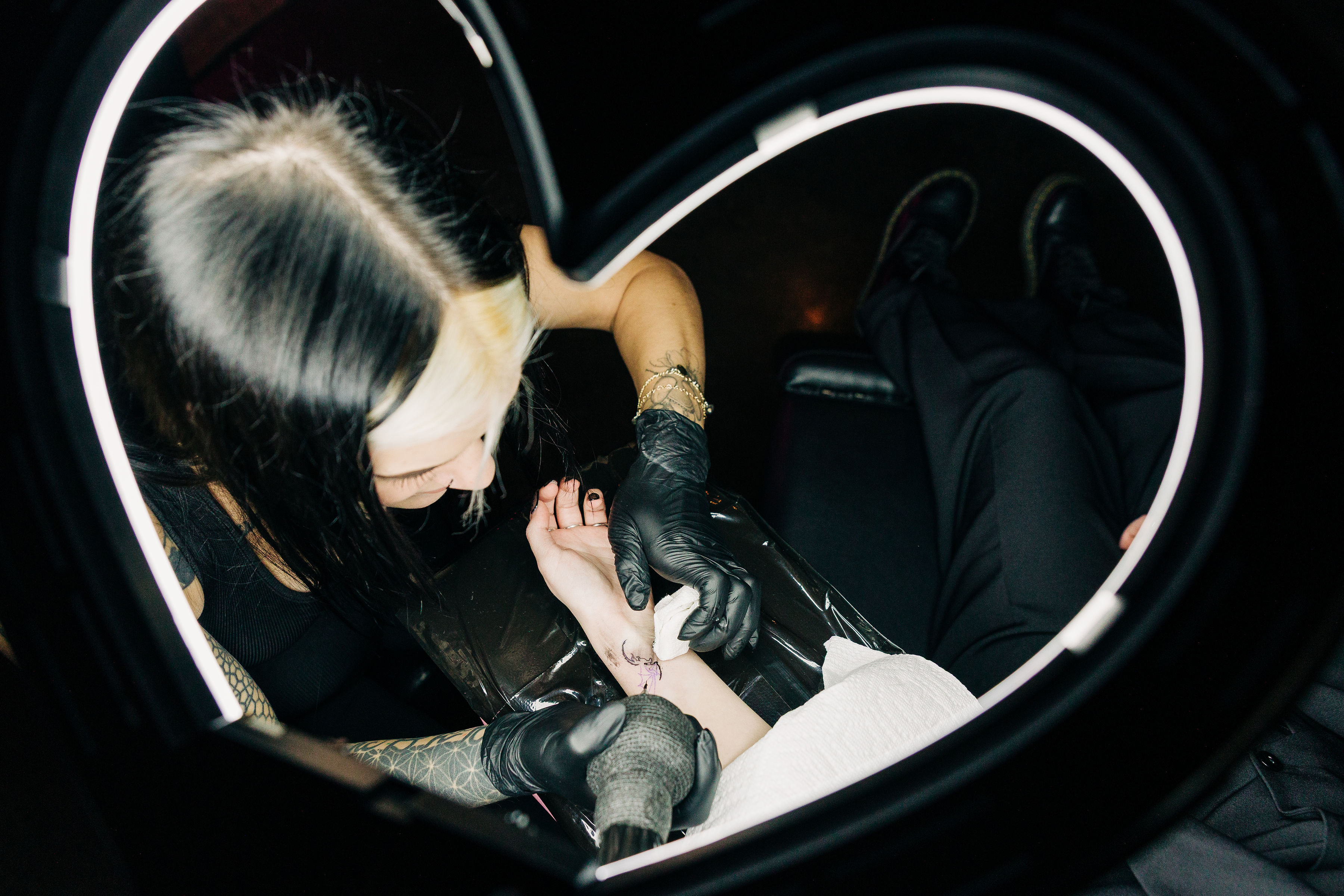 An overhead photo of the tattoo artist tattooing, lit by the heart shape ring light framing the photo.