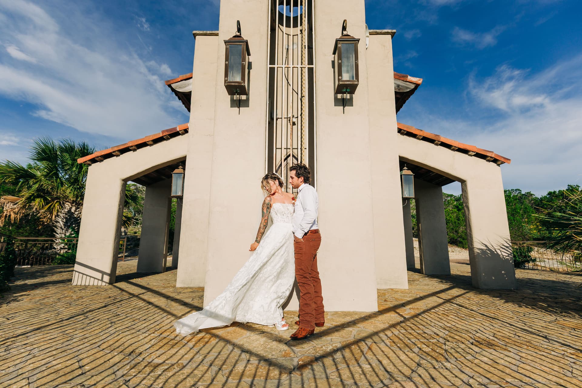 A wide shot of the back of Chapel Dulcenia, with the couple centered and the bride's dress blowing in the wind.