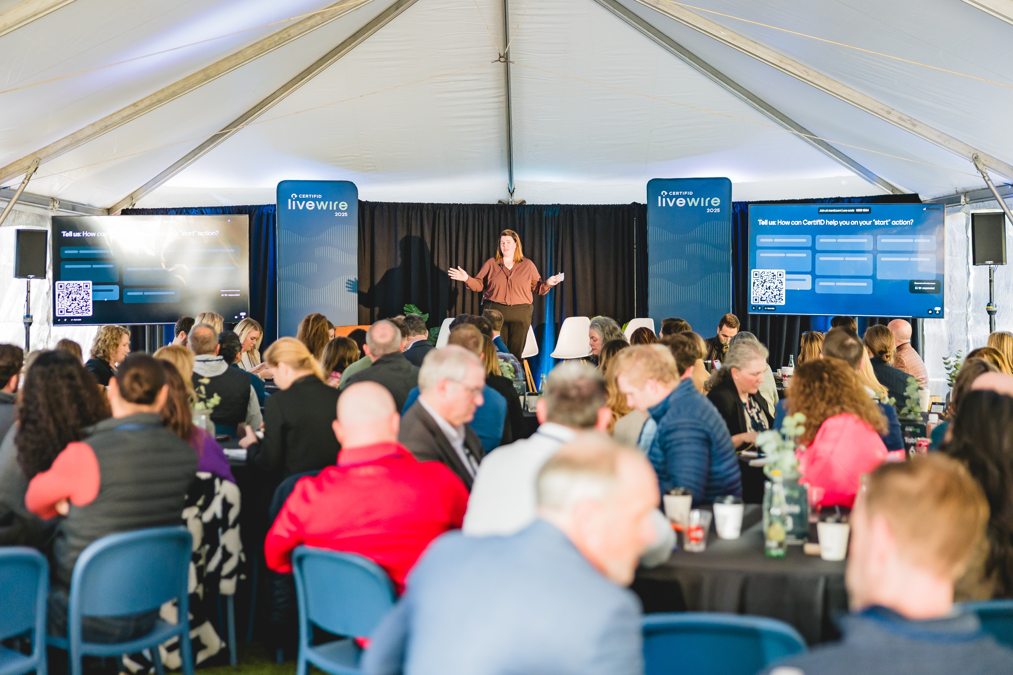 Keynote speaker on stage mid-presentation with an engaged audience visible in the foreground, warm natural lighting