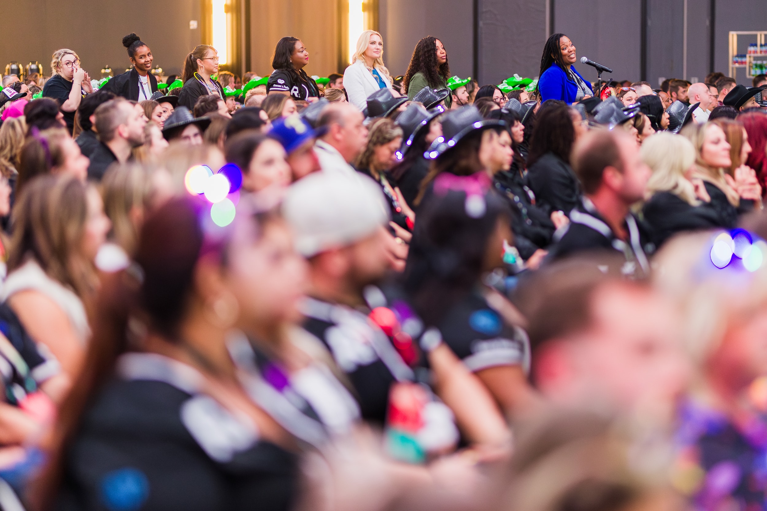 Wide-angle shot of a full, energized corporate event room with attendees mingling, ambient lighting, and employees lined up at a microphone to ask the keynote speaker questions