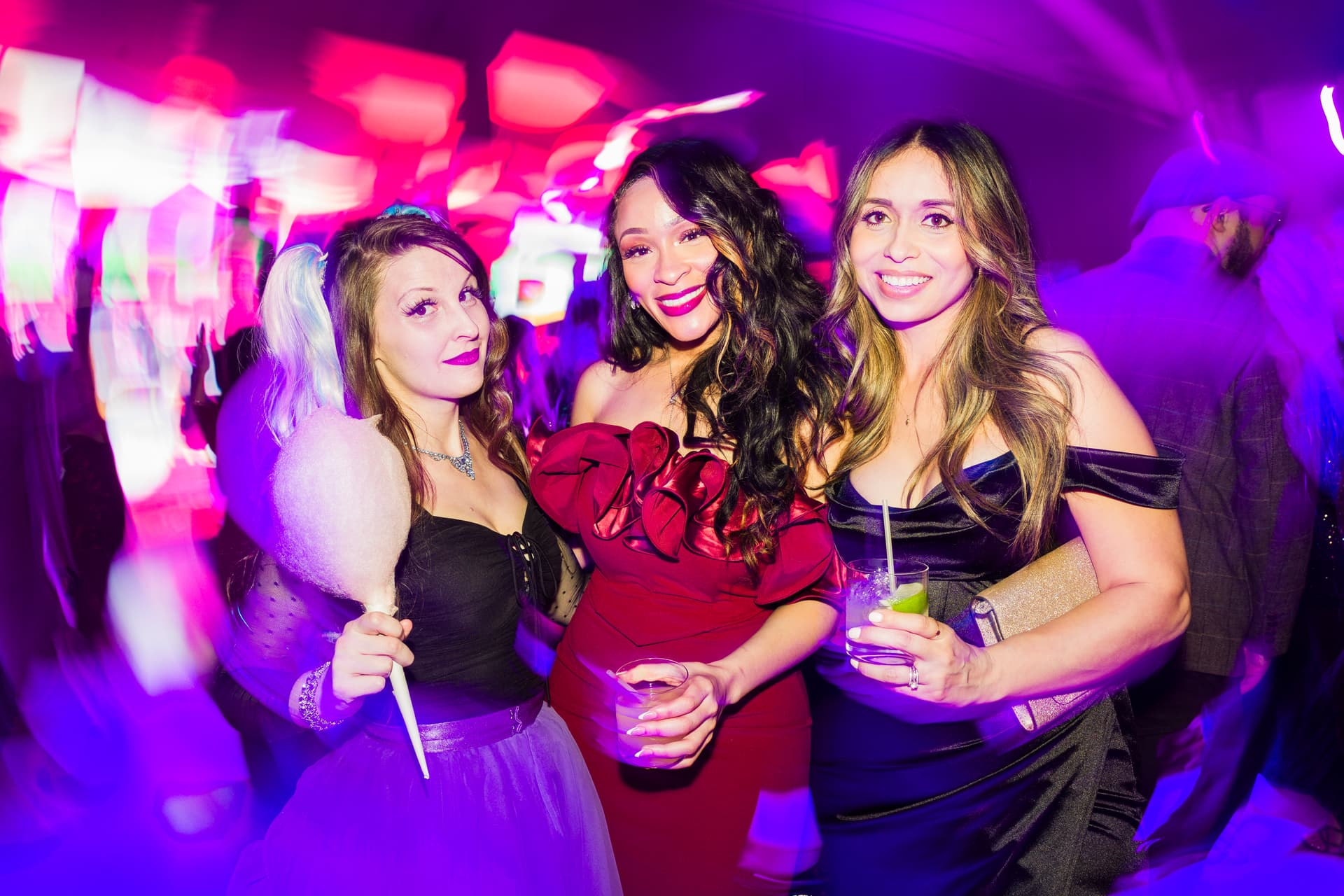 Three women on the dance floor after an awards dinner, smiling toward the camera under colorful lighting