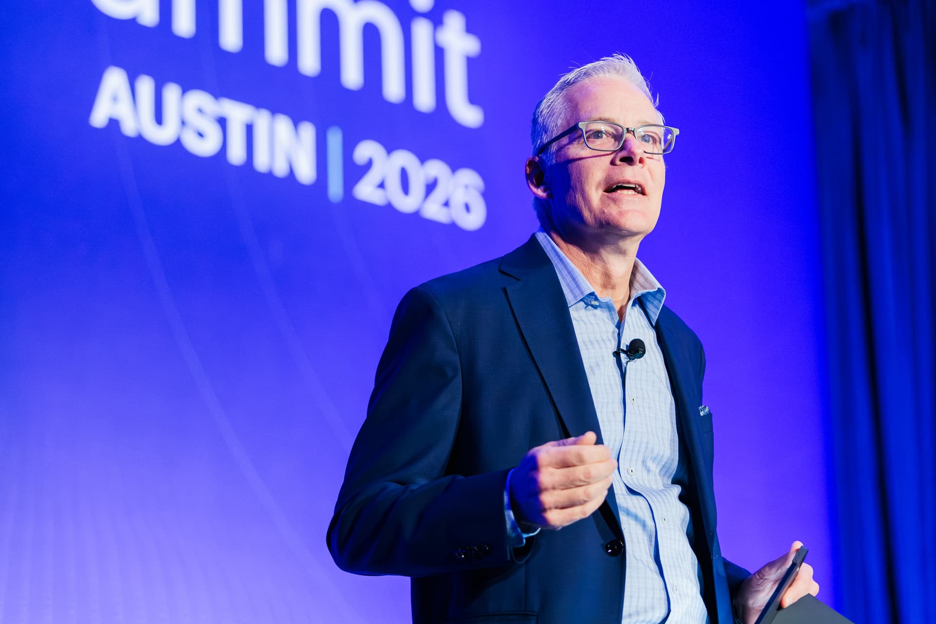 Close-up of a speaker on stage mid-sentence, addressing the audience at an Austin corporate event