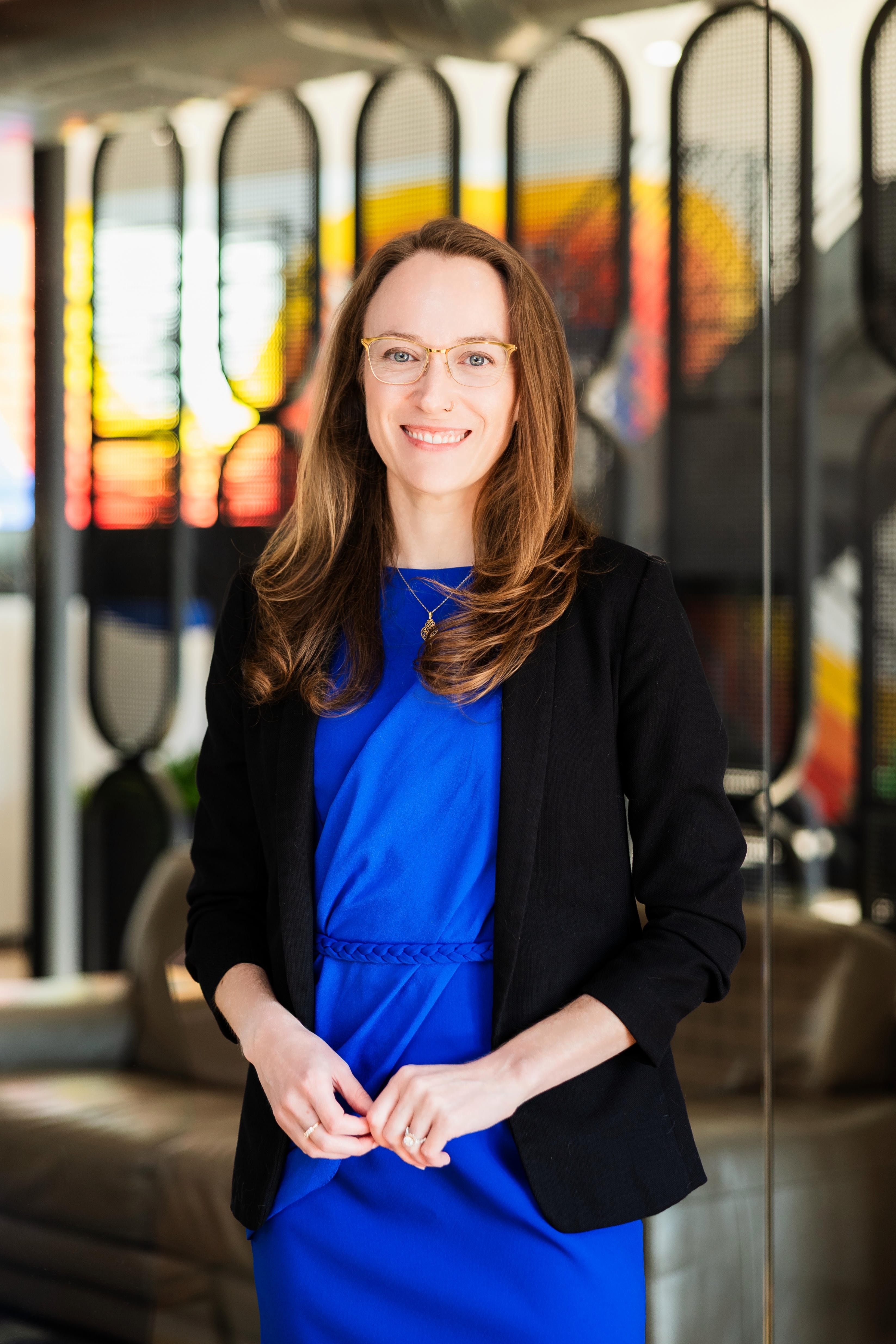 Polished professional headshot of a woman in business attire in her office environment, warm studio lighting highlighting a confident and approachable expression
