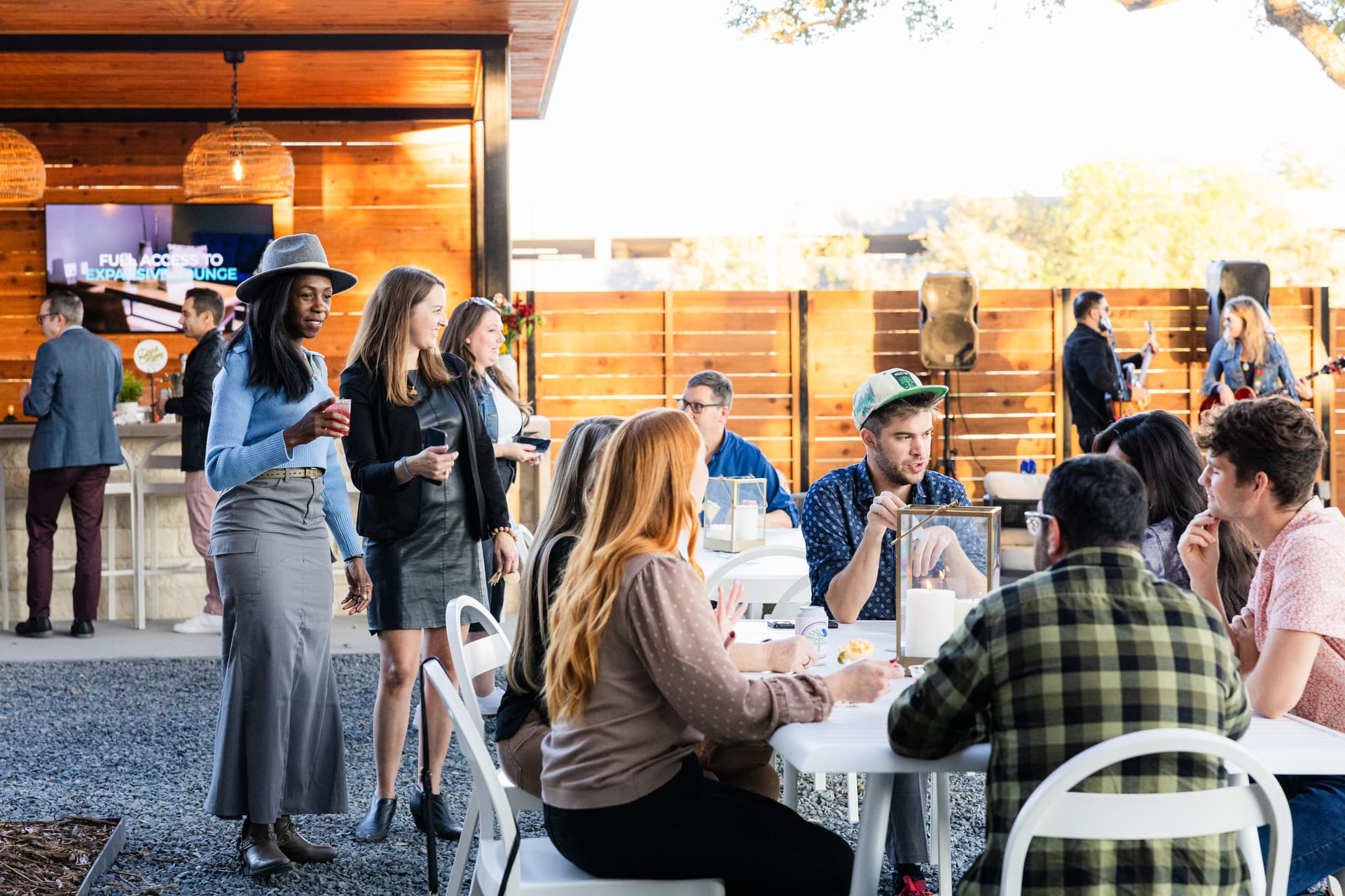 Candid event photography moment showing the photographer blending into the crowd — guests engaged in natural conversation at a corporate cocktail reception, unaware they are being photographed, with warm ambient lighting