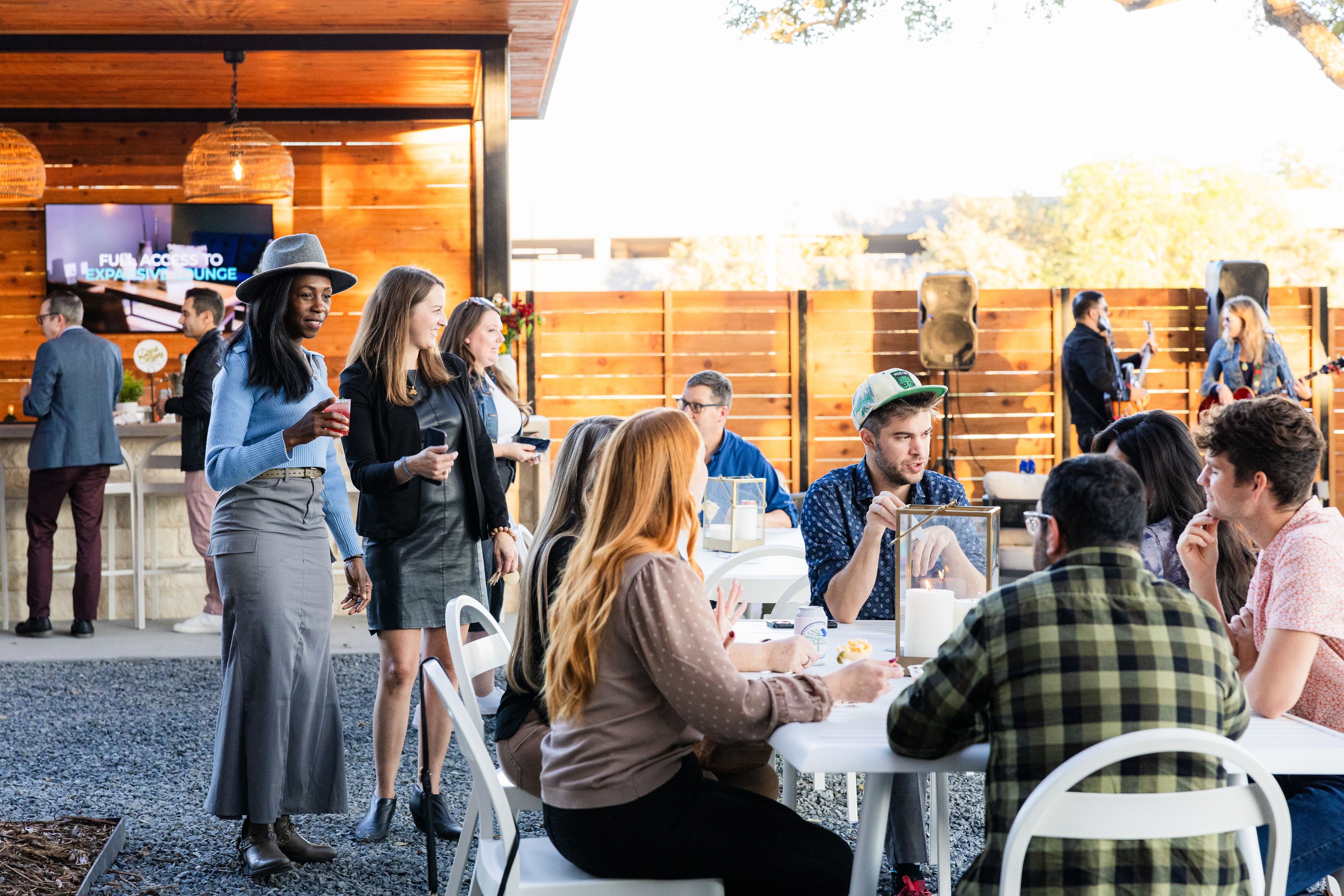 Candid event photography moment showing the photographer blending into the crowd — guests engaged in natural conversation at a corporate cocktail reception, unaware they are being photographed, with warm ambient lighting