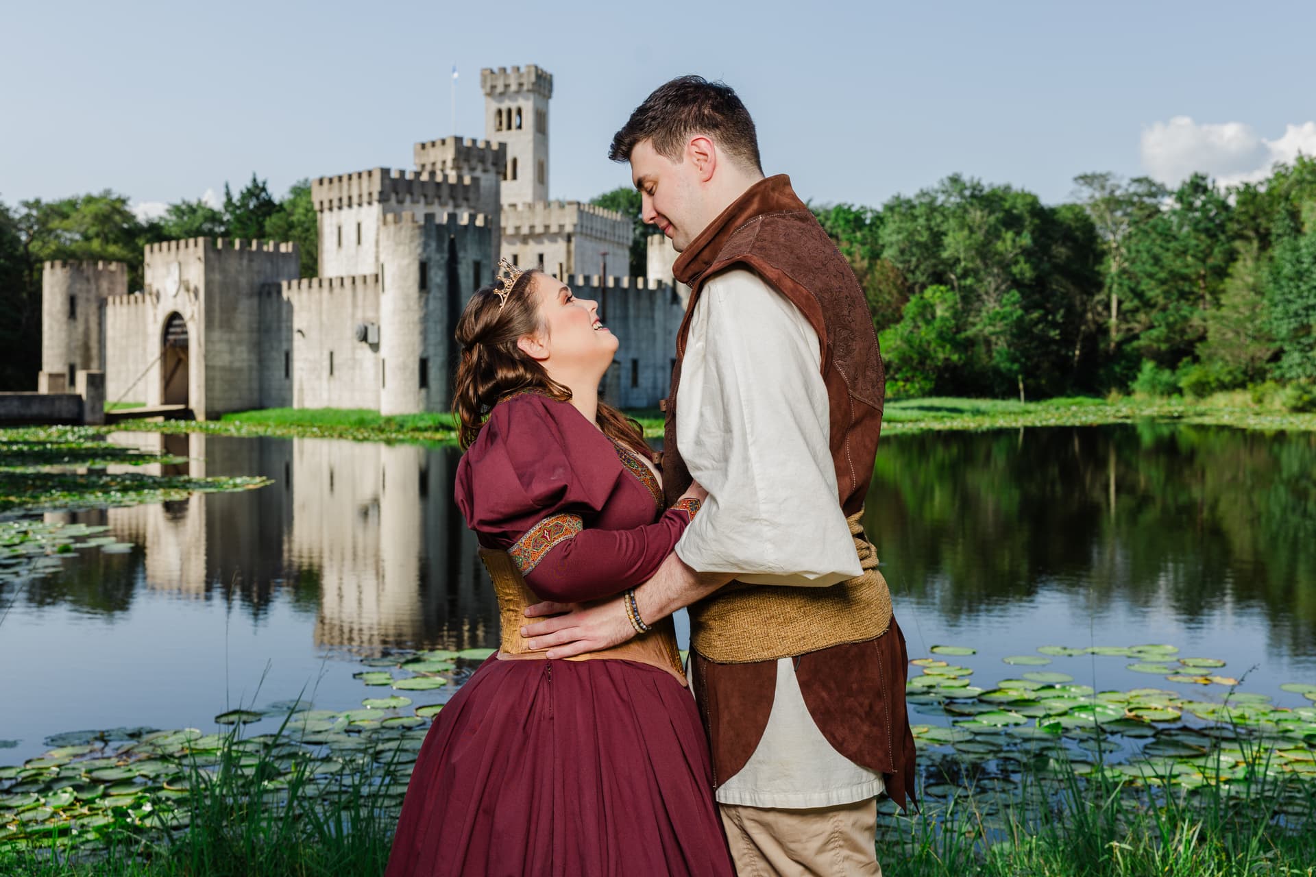 Couple whose outfits perfectly complement their engagement session location — a medieval inspired outfit in front of a castle by the water, showing visual harmony between wardrobe and environment