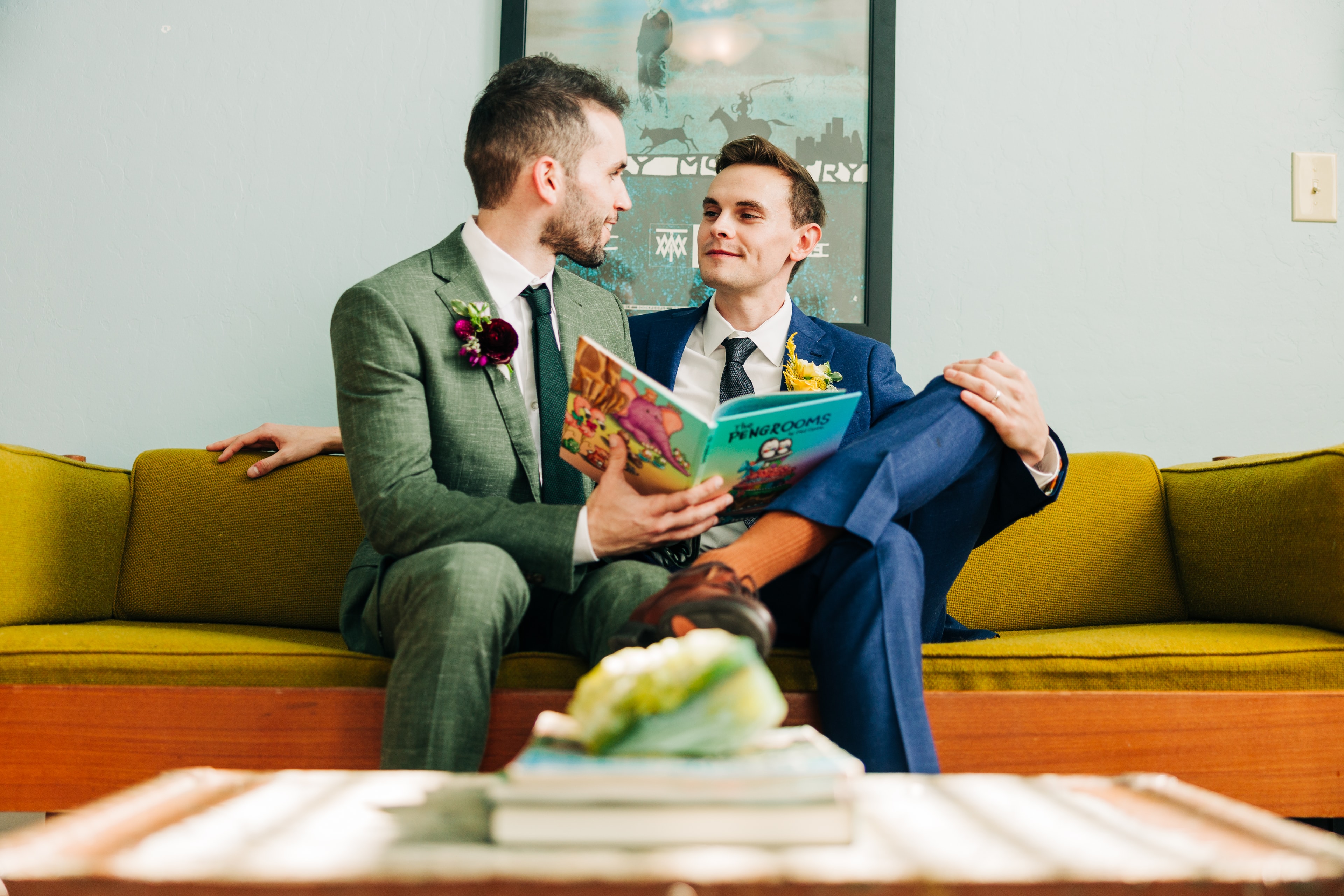 two grooms stealing a quiet private moment together away from guests, intimate and tender. they sit on a couch reading a book together.