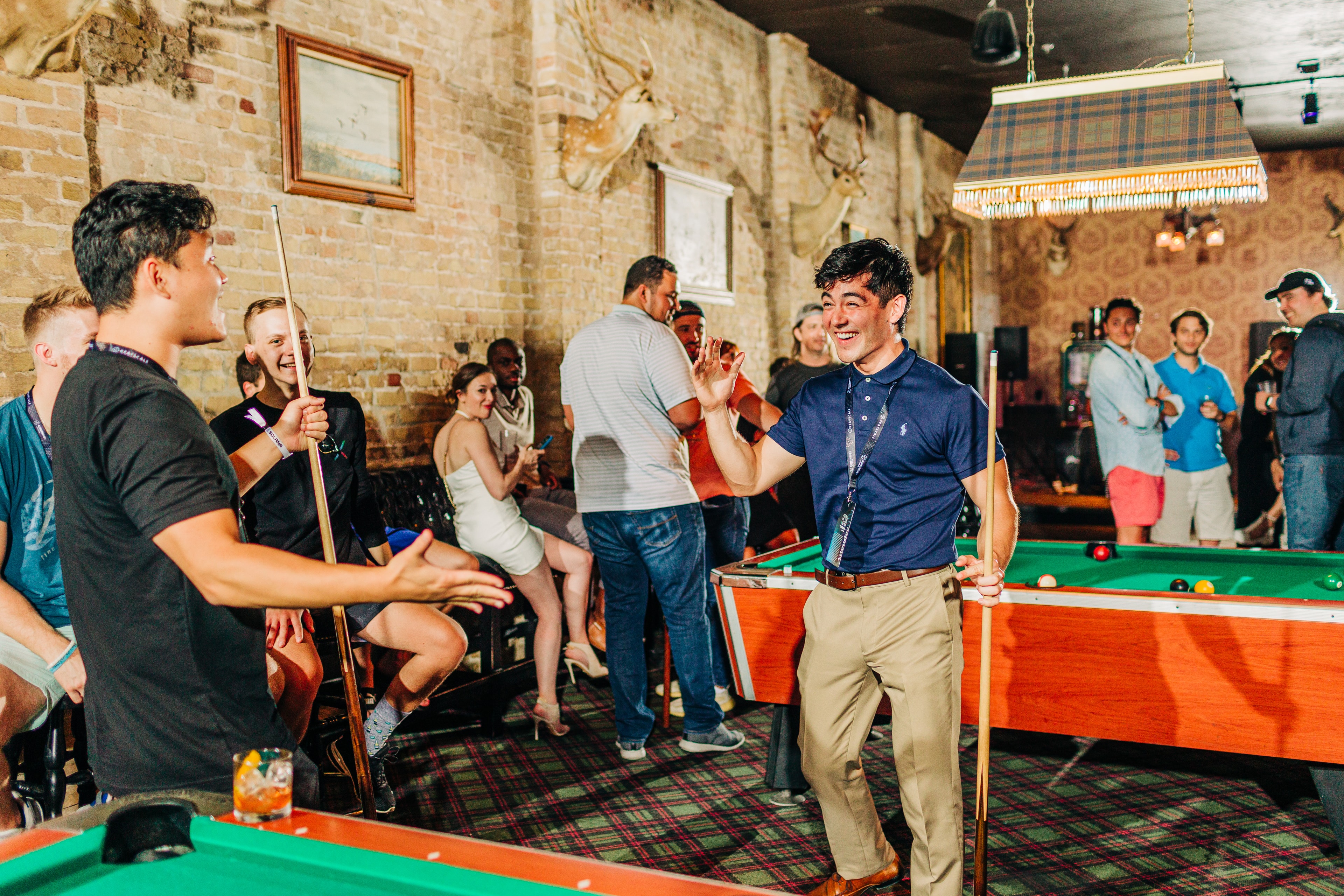 High-energy SXSW party scene with a group celebrating a win at pool at the Seven Grand bar on east 6th street. everyone is wearing their sxsw badges and interacting energetically.