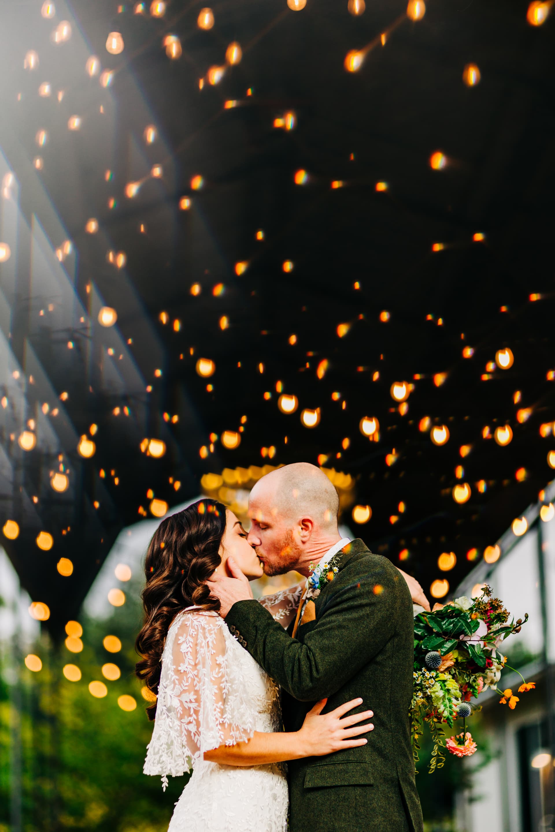 Couple portrait at Springdale Station with the train station backdrop. the couple is surrounded by an array of string lights as they dramatically kiss.